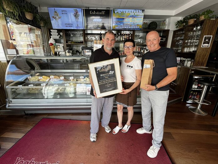 Markus Zlatnik, Irene Jandl und Bürgermeister Georg Rosner stehen nebeneinander im Lokal. Dahinter ist die Eisvitrine zu sehen.