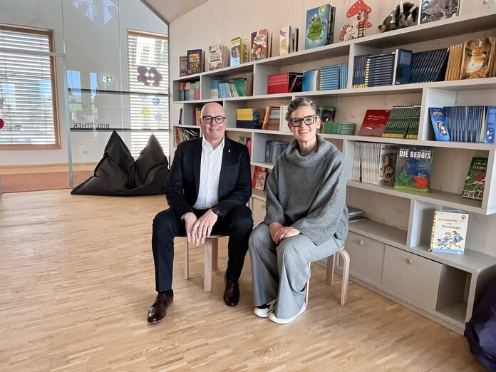 Bürgermeister Georg Rosner und Leiterin Christina Frotschnig sitzen nebeneinander auf Hockern in der Schulbibliothek.