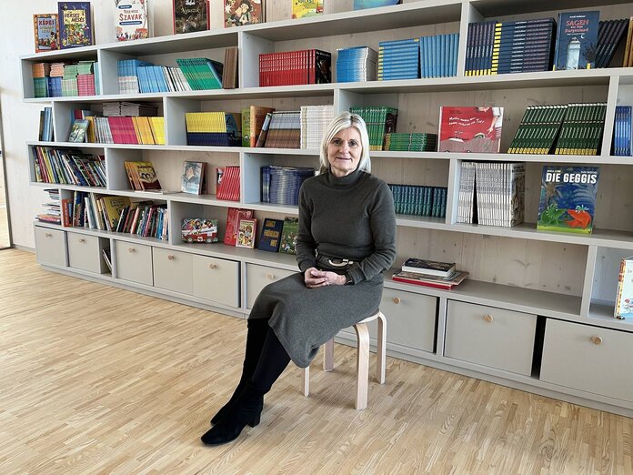 Roswitha Imre sitzt auf einem Hocker in der Bibliothek der Schule.