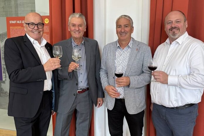 Bürgermeister, Amstleiter a.D., Vizebürgermeister und aktueller Amtsleiter stehen nebeneinander und stoßen mit einem Weinglas auf den Jubilar an.