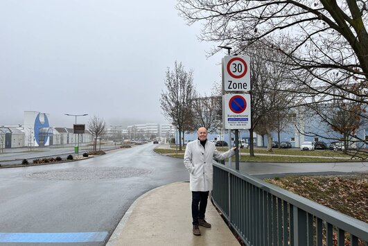 Der Bürgermeister steht auf einer Brücke im Stadtgebiet, daneben steht die Verkehrstafel, die auf die 30-km/h Beschränkung hinweist.
