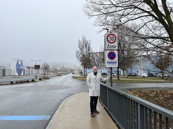 Der Bürgermeister steht auf einer Brücke im Stadtgebiet, daneben steht die Verkehrstafel, die auf die 30-km/h Beschränkung hinweist.