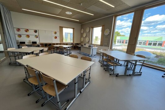 Eine Klasse der neuen Volksschule, jeweils zwei Tische stehen in Gruppen zusammen, durch das Fenster auf der rechten Seite blickt man auf die EMS