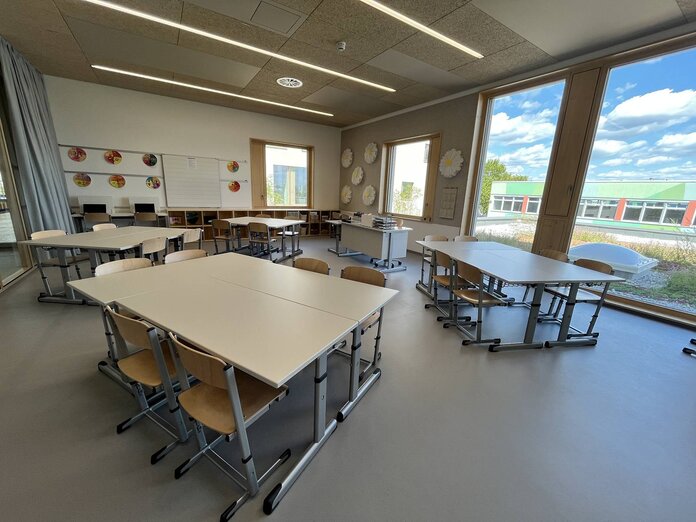 Eine Klasse der neuen Volksschule, jeweils zwei Tische stehen in Gruppen zusammen, durch das Fenster auf der rechten Seite blickt man auf die EMS