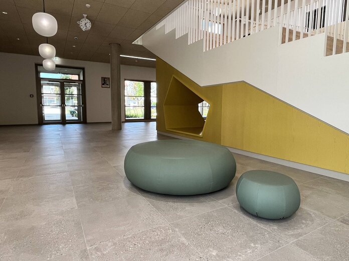 Eingangsbereich mit Blick zur Eingangstür der Musikschule, davor zwei Sitzkissen in türkiser Farbe