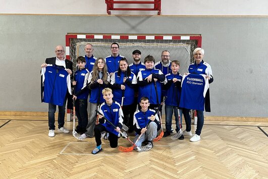 Schüler und Pädagogen der Floorballteams mit Bürgermeister Georg Rosner, dieser hält eine Jacke in der Hand und präsentiert sie.