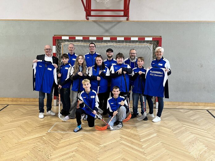 Schüler und Pädagogen der Floorballteams mit Bürgermeister Georg Rosner, dieser hält eine Jacke in der Hand und präsentiert sie.