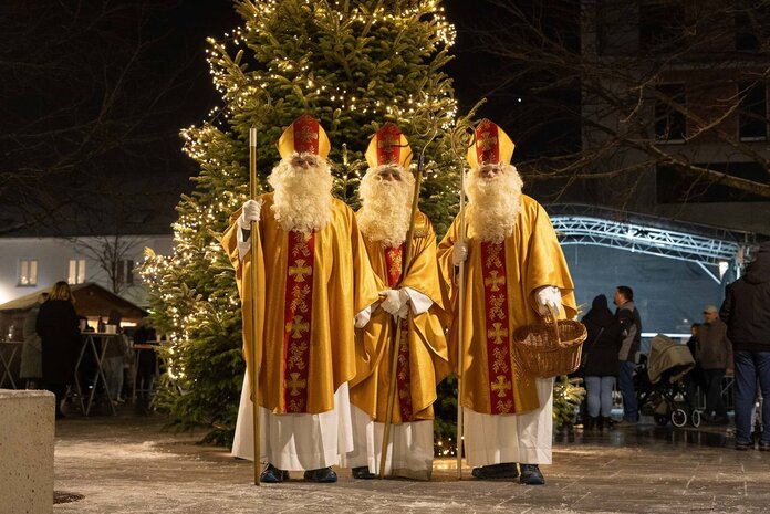 Drei Männer, die als Nikolaus verkleidet sind stehen im Stadtgarten nebeneinander, dahinter ist der beleuchtete Weihnachtsbaum zu sehen.