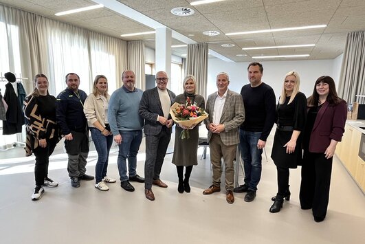 Roswitha Imre steht im Konferenzzimmer und hält einen Blumenstrauß in der Hand, zu ihrer Linken und Rechten stehen die Vertreter der Stadtgemeinde.