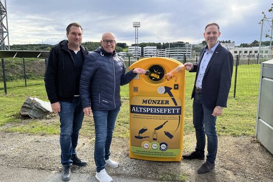 Wirtschaftshofleiter, Bürgermeister und UDB-Geschäftsführer stehen bei einer Münzer Box und werfen eine Flasche mit Altöl in die Box