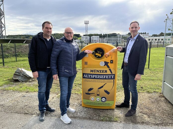 Wirtschaftshofleiter, Bürgermeister und UDB-Geschäftsführer stehen bei einer Münzer Box und werfen eine Flasche mit Altöl in die Box
