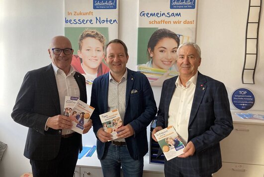 Bürgermeister, Schülerhilfe-Inhaber und Vizebürgermeister stehen nebeneinander, in den Händen halten sie Informationsfolder.